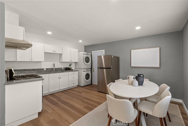 kitchen featuring wood finished floors, freestanding refrigerator, a sink, under cabinet range hood, and stacked washer / dryer