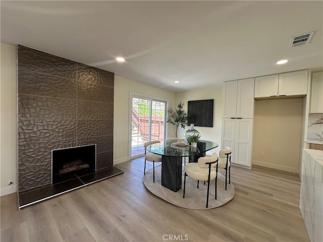 dining room featuring visible vents, light wood-style flooring, a tiled fireplace, recessed lighting, and baseboards