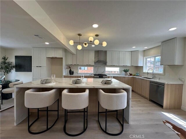 kitchen featuring light stone counters, light wood-style flooring, stainless steel dishwasher, wall chimney exhaust hood, and a sink