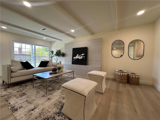 living area featuring visible vents, beam ceiling, baseboards, and wood finished floors