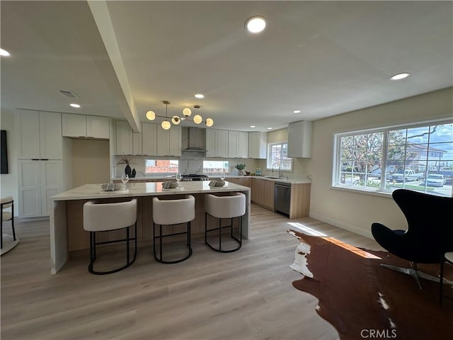 kitchen featuring visible vents, dishwasher, a kitchen breakfast bar, light wood-style floors, and wall chimney exhaust hood