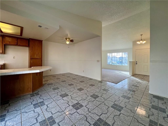 kitchen featuring visible vents, open floor plan, tile countertops, brown cabinetry, and a textured ceiling