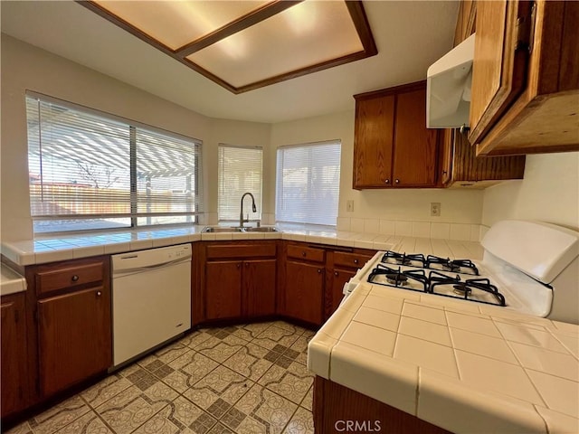 kitchen featuring white appliances, tile counters, range hood, and a sink