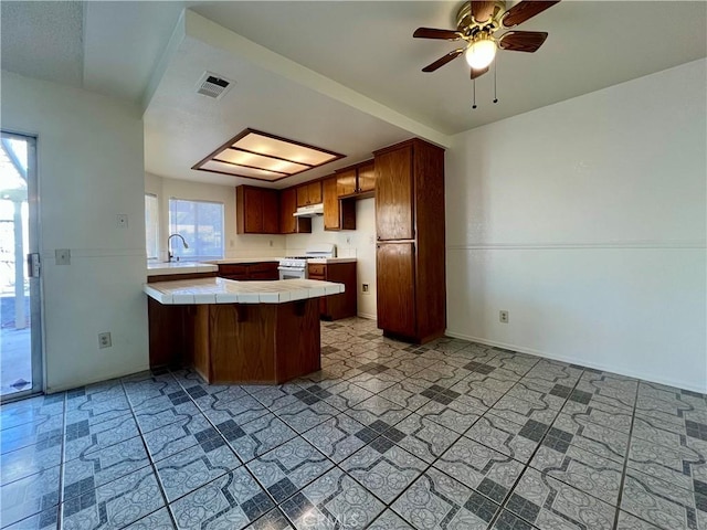 kitchen with visible vents, white range with gas cooktop, under cabinet range hood, tile countertops, and a peninsula