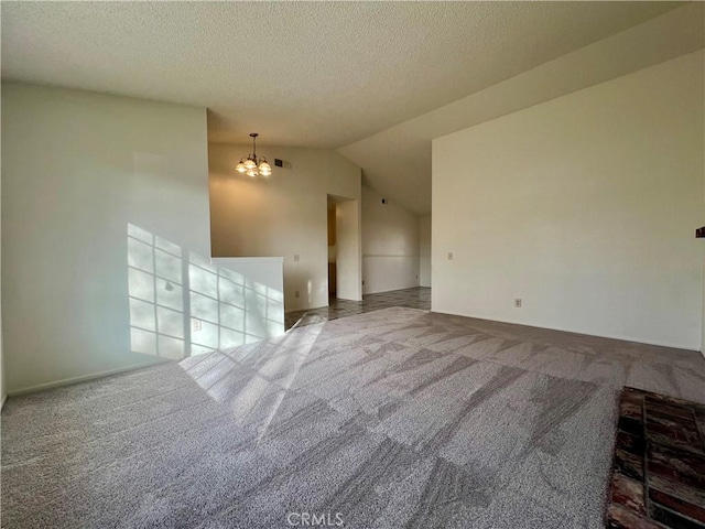 empty room featuring visible vents, lofted ceiling, a textured ceiling, carpet flooring, and a notable chandelier