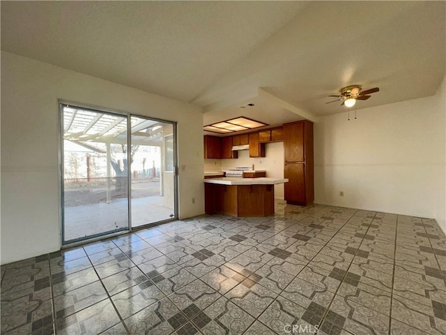 kitchen with ceiling fan, gas range, light countertops, lofted ceiling, and brown cabinets