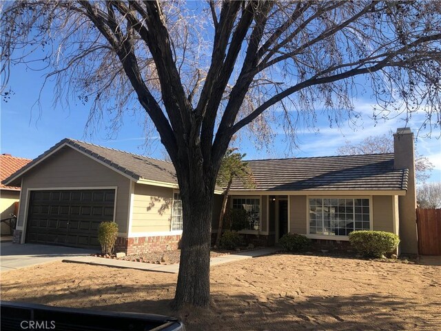 ranch-style home with brick siding, fence, concrete driveway, a chimney, and a garage