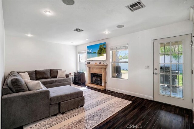 living area with baseboards, dark wood-style floors, visible vents, and a fireplace with raised hearth