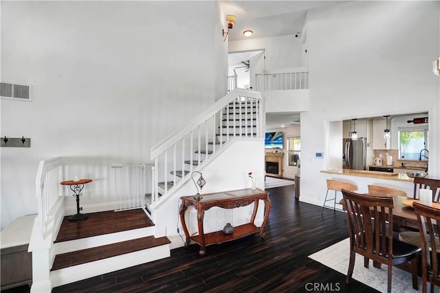 dining space featuring stairway, wood finished floors, visible vents, a high ceiling, and a fireplace with raised hearth