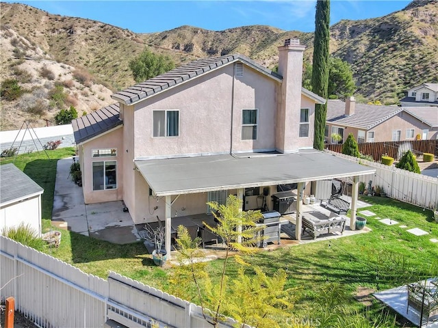 back of house with a fenced backyard, stucco siding, a lawn, a patio area, and a mountain view