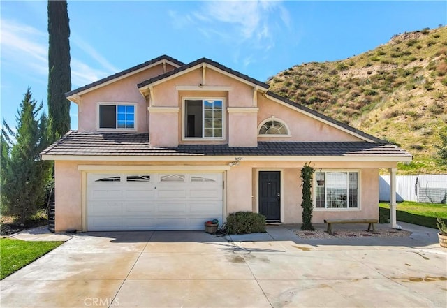 traditional home featuring an attached garage, fence, driveway, and stucco siding