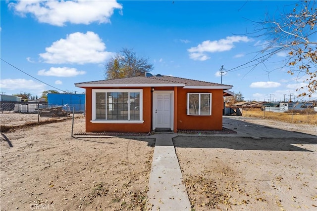 bungalow-style home with stucco siding and fence