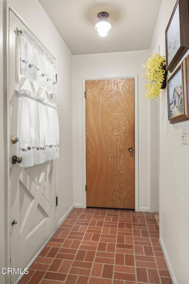 entryway featuring brick floor and baseboards