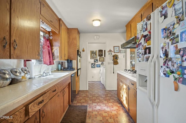 kitchen featuring under cabinet range hood, tile countertops, independent washer and dryer, white appliances, and a sink