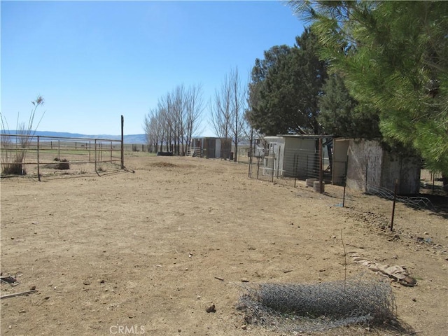 view of yard featuring fence, an outbuilding, exterior structure, and a rural view