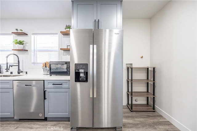 kitchen with a sink, gray cabinets, appliances with stainless steel finishes, light wood-style floors, and open shelves