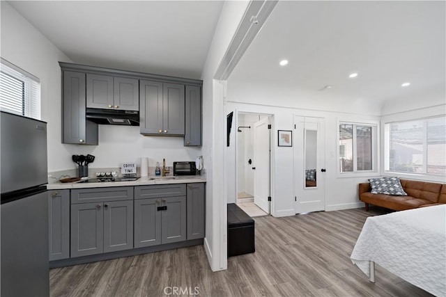 kitchen featuring a wealth of natural light, gray cabinets, under cabinet range hood, freestanding refrigerator, and black electric stovetop