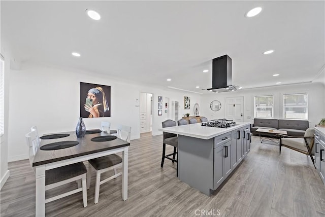 kitchen featuring gray cabinetry, a center island, range hood, a kitchen breakfast bar, and gas cooktop