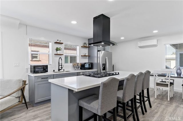 kitchen featuring island exhaust hood, a sink, an AC wall unit, stainless steel refrigerator with ice dispenser, and black microwave