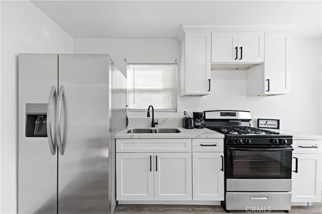 kitchen with appliances with stainless steel finishes, white cabinetry, light countertops, and a sink