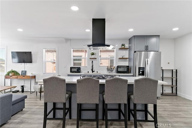 kitchen featuring black microwave, light countertops, light wood-style flooring, island exhaust hood, and open shelves