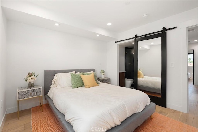bedroom featuring recessed lighting, a barn door, baseboards, and light wood-style flooring