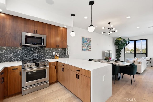 kitchen with light wood-type flooring, appliances with stainless steel finishes, a peninsula, and decorative backsplash