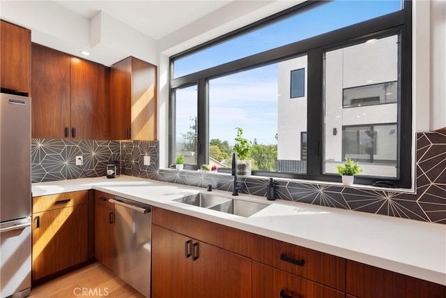 kitchen featuring tasteful backsplash, light countertops, brown cabinets, stainless steel appliances, and a sink