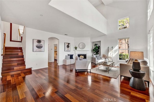 living room with stairs, wood finished floors, a wealth of natural light, and a lit fireplace