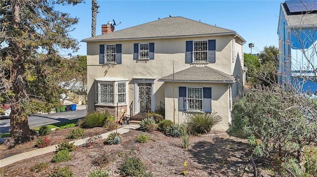 traditional home with a shingled roof, stucco siding, and a chimney