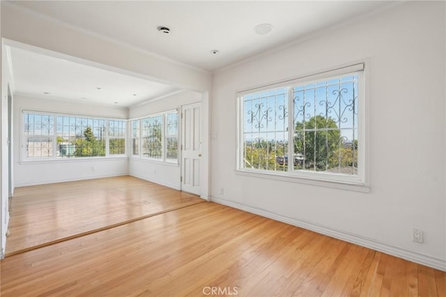 empty room featuring crown molding, baseboards, and wood-type flooring