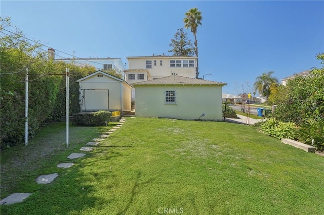 rear view of house with an outbuilding, fence, stucco siding, a storage unit, and a lawn