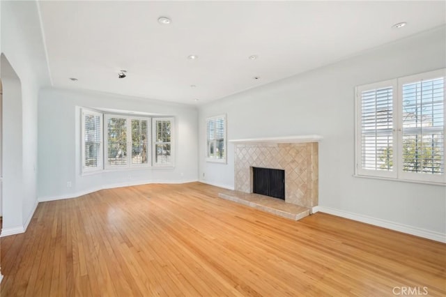 unfurnished living room featuring light wood-type flooring, recessed lighting, arched walkways, a fireplace, and baseboards