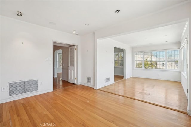 unfurnished room featuring light wood-type flooring, visible vents, and arched walkways