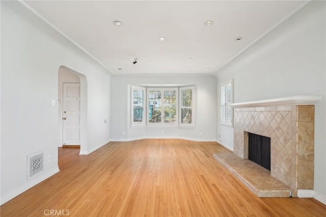 unfurnished living room featuring arched walkways, visible vents, a fireplace, and light wood-type flooring