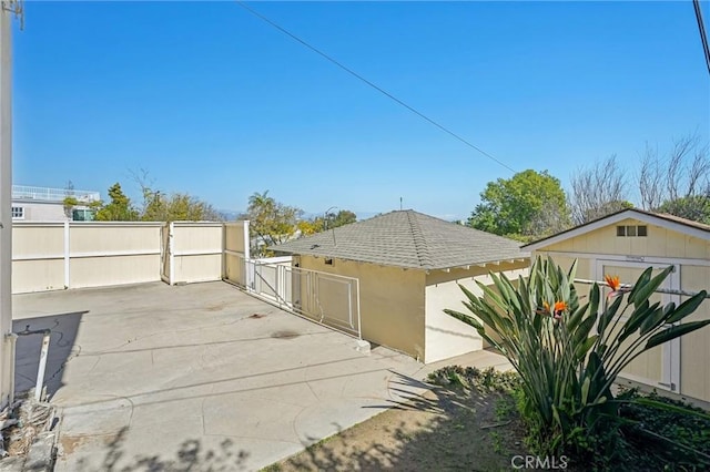 view of side of home featuring a shingled roof, fence, and a gate