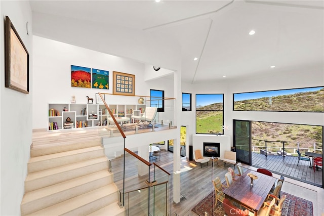 living room with stairway, wood finished floors, high vaulted ceiling, recessed lighting, and a lit fireplace