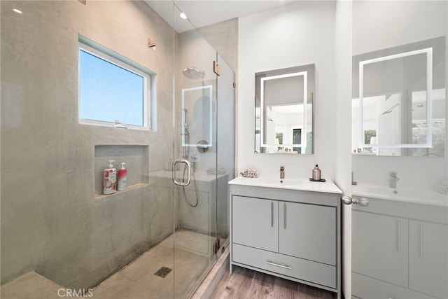 full bathroom featuring a sink, a stall shower, two vanities, and wood finished floors