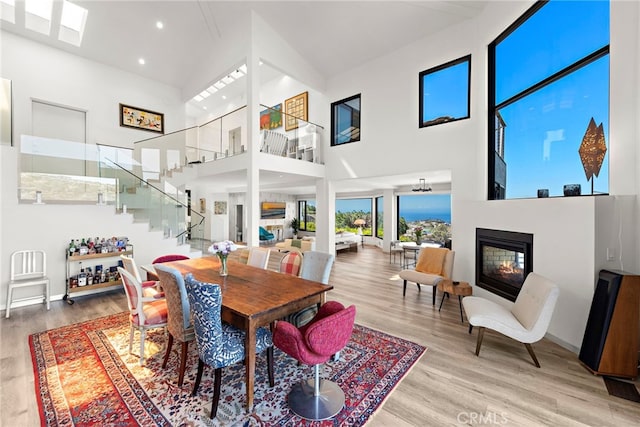 dining room featuring wood finished floors, recessed lighting, stairs, a towering ceiling, and a glass covered fireplace