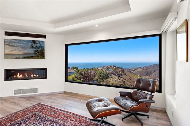 living area featuring visible vents, a raised ceiling, a water view, and wood finished floors