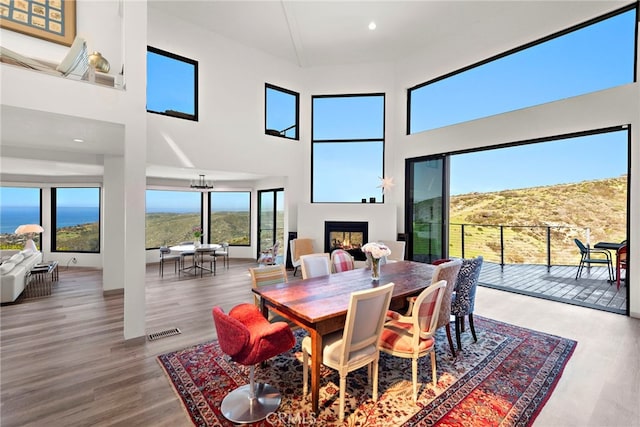 dining space featuring visible vents, a lit fireplace, recessed lighting, a high ceiling, and wood finished floors