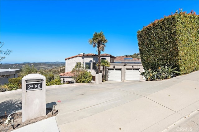 mediterranean / spanish home featuring an attached garage, concrete driveway, a tiled roof, a mountain view, and roof mounted solar panels