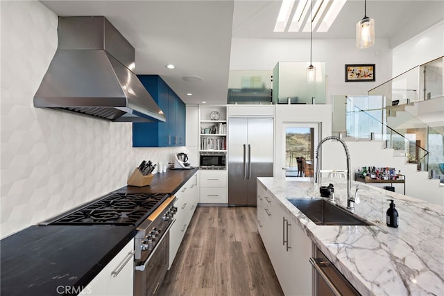 kitchen featuring a sink, open shelves, wood finished floors, wall chimney range hood, and built in appliances