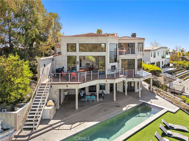 rear view of house featuring stucco siding, stairs, fence, a balcony, and a chimney