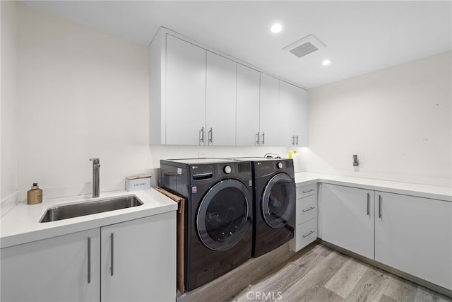 laundry room with light wood-type flooring, visible vents, a sink, washing machine and dryer, and cabinet space