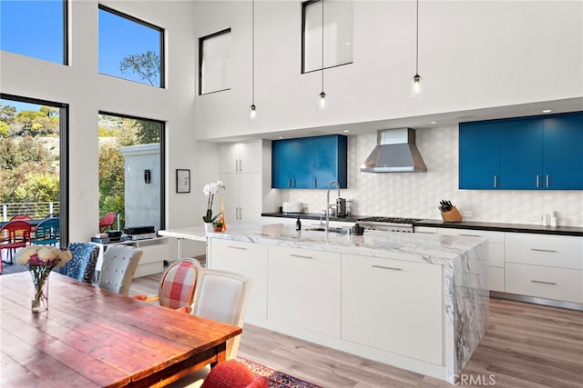 kitchen with a kitchen island with sink, a sink, light wood-style floors, wall chimney range hood, and modern cabinets