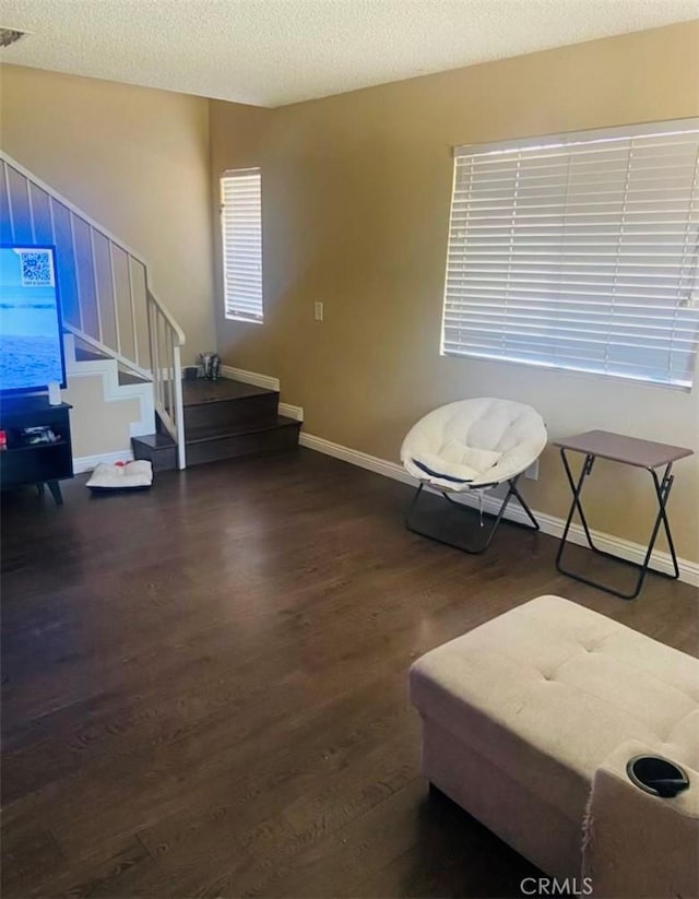 sitting room with stairs, wood finished floors, baseboards, and a textured ceiling