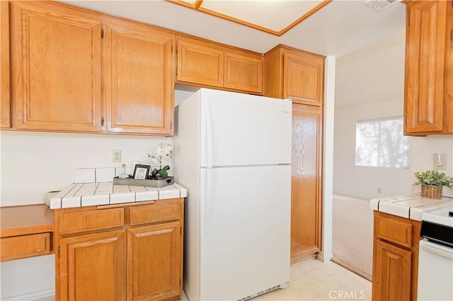 kitchen featuring tile counters, light floors, and freestanding refrigerator