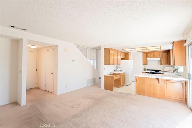 kitchen featuring visible vents, light carpet, freestanding refrigerator, tile countertops, and range