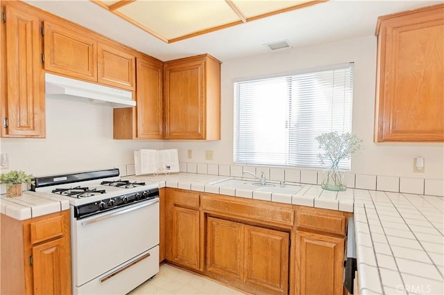 kitchen with visible vents, under cabinet range hood, tile countertops, white gas range, and a sink